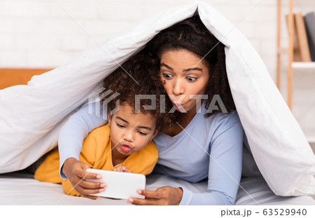African Mom And Little Girl Playing Mobile Games In Bed 63529940