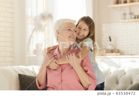 Family bonding. Lovely little girl happily emracing her grandma in light living room 63530472