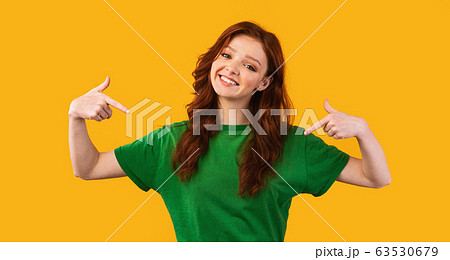 Smiling Red-Haired Girl Pointing Fingers At Herself Over Yellow Background 63530679