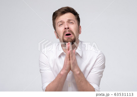 Emotive guy clenching hands together frowning Emotive guy clenching hands together frowning 63531113