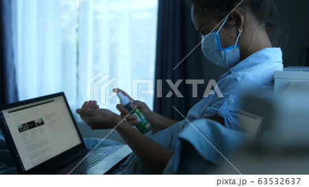 Woman in mask by computer quarantined at home during a pandemic. A woman treats hands with an antiseptic and works on notebook. Woman in mask by computer quarantined at home during a pandemic. A woman treats hands with an antiseptic and works on notebook. 63532637