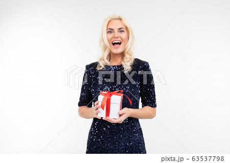 blond Caucasian woman in a blue shiny dress joyfully holds a received gift box on a white background blond Caucasian woman in a blue shiny dress joyfully holds a received gift box on a white background 63537798
