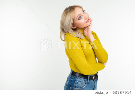 girl in a yellow blouse and jeans looks thoughtfully at a white studio background 63537914