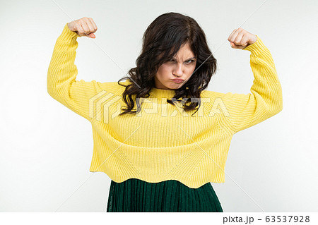 charming brunette lady in a yellow sweater and green skirt shows muscles raising her hands up on a charming brunette lady in a yellow sweater and green skirt shows muscles raising her hands up on a 63537928