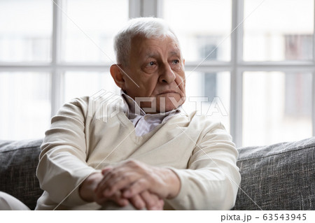 Pensive old man sitting on couch in living room alone 63543945