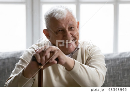 Positive old grandfather holding walking stick resting on couch Positive old grandfather holding walking stick resting on couch 63543946