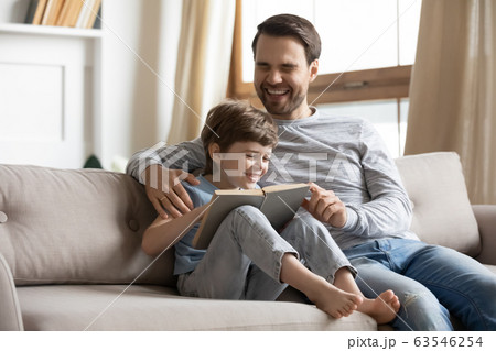 Smiling young dad and little son reading book together Smiling young dad and little son reading book together 63546254