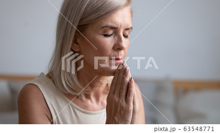 Focused faithful mature woman praying with closed eyes. Focused faithful mature woman praying with closed eyes. 63548771