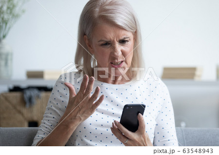 Unhappy middle aged lady irritated by bad smartphone work. 63548943