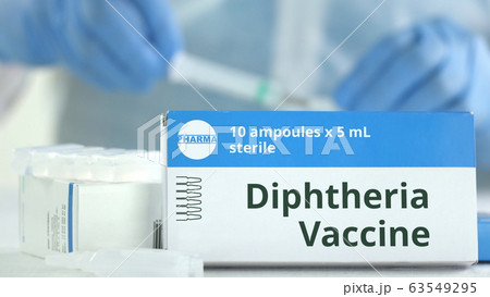 Box with diphtheria vaccine on the table against blurred lab assistant. Fictional phaceutical logo 63549295