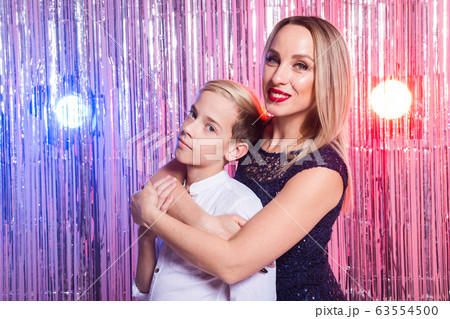 Mothers day, children and family concept - teen boy hugging his mom on shiny party background. 63554500