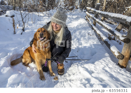 Smiling senior woman petting dog in snow Smiling senior woman petting dog in snow 63556331