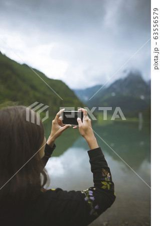 Young woman photographing mountain and lake with smartphone 63556579