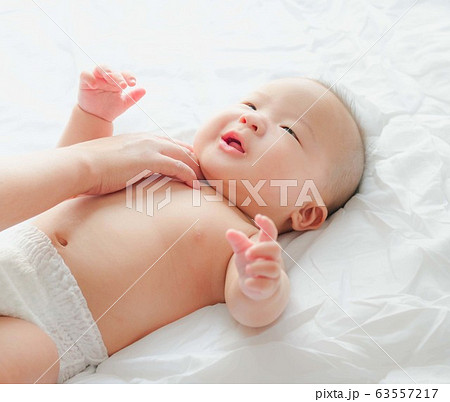Portrait of a newborn Asian baby on the bed drinks milk from a bottle, Charming black-eyed baby 4 month old lies in bed ,A child resting on a bed 63557217
