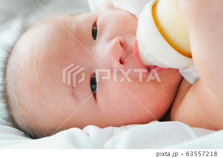 Portrait of a newborn Asian baby on the bed drinks milk from a bottle, Charming black-eyed baby 4 month old lies in bed ,A child resting on a bed 63557218