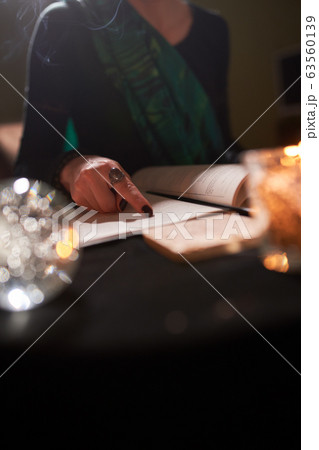 Close-up of female fortune-teller's hands, book of predictions, burning candle Close-up of female fortune-teller's hands, book of predictions, burning candle 63560139