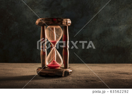 Time is running out concept. An hourglass with sand falling through, on a dark background with a place for text, toned image 63562292