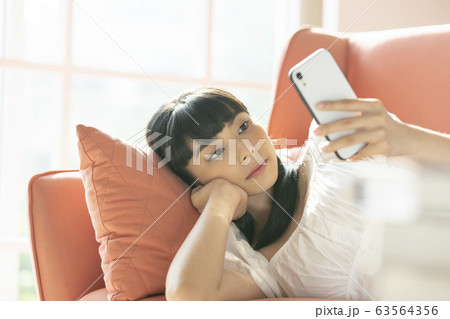 ソファーでスマホを操作する若い女性 63564356
