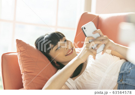ソファーでスマホを操作する若い女性 ソファーでスマホを操作する若い女性 63564578