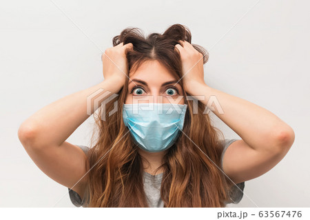 Scared young woman in medical mask standing over white wall Scared young woman in medical mask standing over white wall 63567476
