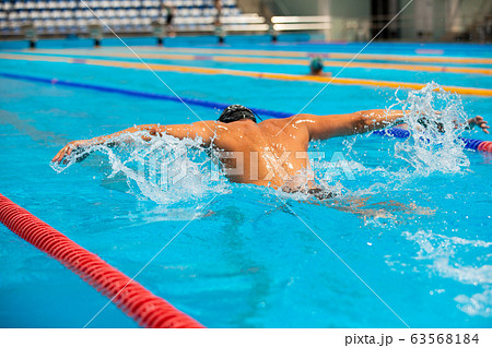 Athletic man swimming in butterfly style in the swimming pool with clear blue water. 63568184
