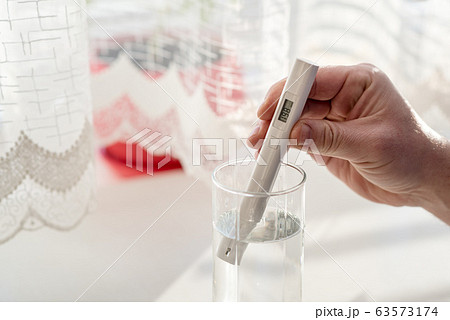 Process of checking the purity level of tap water using water TDS meter tool, close up. Device shows 198 ppm of contaminant level, which is considered the typical value. At home in the kitchen 63573174