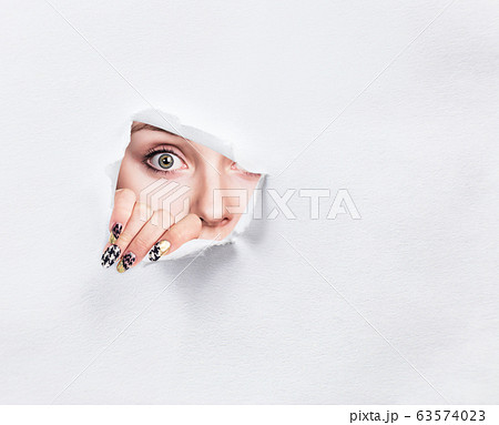 Surprised woman peeps into the slit of white paper. 63574023
