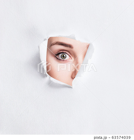 Surprised woman peeps into the slit of white paper. 63574039