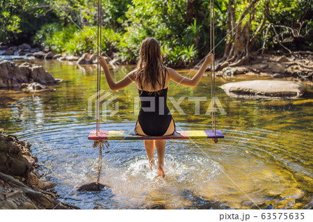 Beautiful happy girl, young pretty cheerful woman traveler sitting, swinging on a swing tied to a 63575635