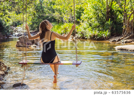 Beautiful happy girl, young pretty cheerful woman traveler sitting, swinging on a swing tied to a 63575636