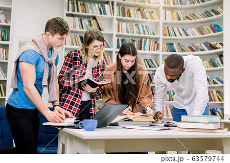 Group portrait of creative modern multiracial friends university students, preparing for exams in the library, using laptop, books and writing notes. Education and library concept 63579744