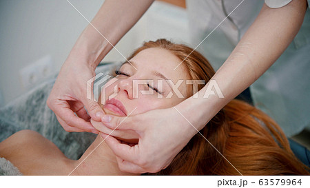 Massage - woman massage therapist massaging the face of a red-haired woman Massage - woman massage therapist massaging the face of a red-haired woman 63579964