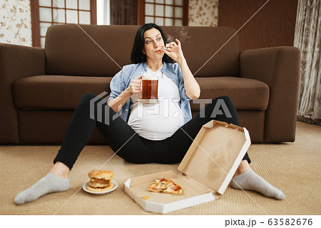 Pregnant woman with belly smoking and drinks beer 63582676