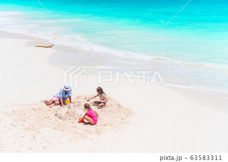 Father and little daughters making sand castle at tropical beach Father and little daughters making sand castle at tropical beach 63583311
