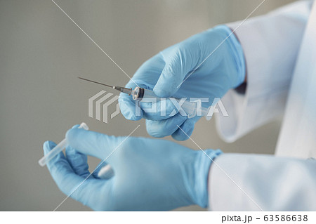 Person in a white uniform holding a syringe in her hands Person in a white uniform holding a syringe in her hands 63586638