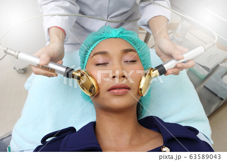 Treatment on Asian Woman as patient to make skin smooth bright and cure acne with medical beauty device instrument golden spoon on face in hospital clinic Treatment on Asian Woman as patient to make skin smooth bright and cure acne with medical beauty device instrument golden spoon on face in hospital clinic 63589043