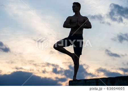 Fit young man practices sun salutation yoga on the edge of cliff at sunset Fit young man practices sun salutation yoga on the edge of cliff at sunset 63604605
