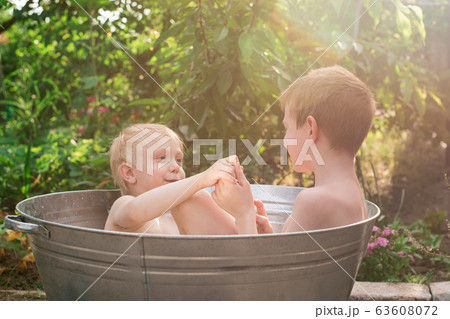 Two brothers bathing in metal basin in village Two brothers bathing in metal basin in village 63608072