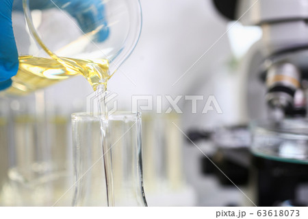 Scientist hand wearing protective gloves pouring some yellow liquid at laboratory 63618073