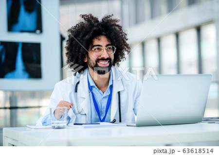 Portrait of cheerful male doctor sitting in hospital, using laptop. 63618514