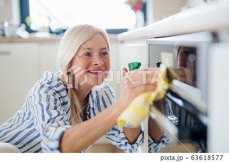Portrait of senior woman cleaning kitchen cabinet doors indoors at home. Portrait of senior woman cleaning kitchen cabinet doors indoors at home. 63618577
