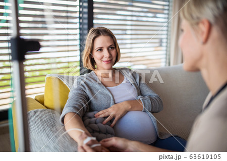 Healthcare worker with IV drip examining pregnant woman indoors at home. Healthcare worker with IV drip examining pregnant woman indoors at home. 63619105