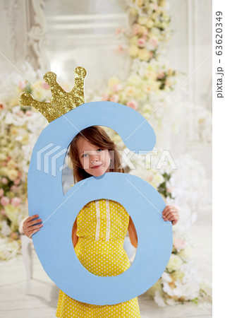 A girl in a yellow dress holds a large number 6.With a Golden crown. The Princess birthday party. A girl in a yellow dress holds a large number 6.With a Golden crown. The Princess birthday party. 63620349