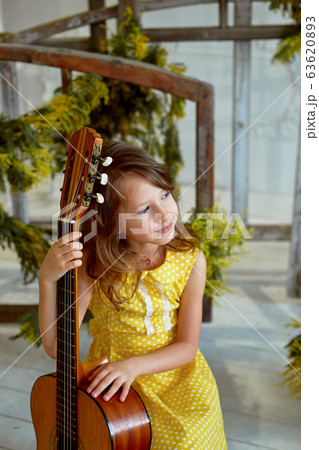 Girl, 6 years old.Her hair is loose. Yellow dress, Mimosa, beautiful interior. Laughing and holding a guitar. Music lesson. 63620893