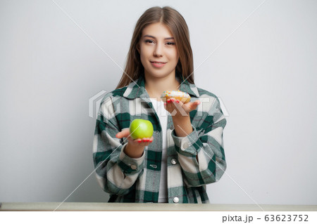 Cute woman makes a choice between healthy and harmful food 63623752