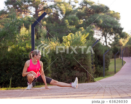 Fit caucasian blond woman do warming up before jogging on the footpath outdoor in summer among greenery, selective focus. 63626030