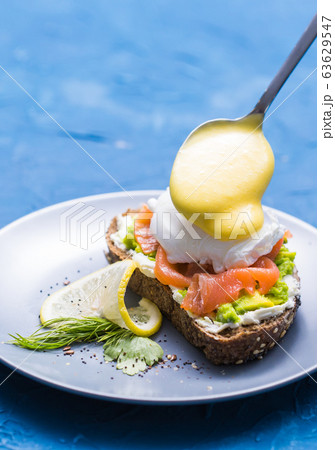Morning and breakfast concept - Preparation of sandwich with salmon, spoon is pouring sauce on it. Morning and breakfast concept - Preparation of sandwich with salmon, spoon is pouring sauce on it. 63629547
