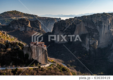 Aerial view of monastery Rousanou and breathtaking picturesque valley and landmark canyon of Meteora at sunset, Kalambaka, Greece, shadows, twisted road, bridge Aerial view of monastery Rousanou and breathtaking picturesque valley and landmark canyon of Meteora at sunset, Kalambaka, Greece, shadows, twisted road, bridge 63630419
