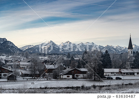 Aerial view of the small cozy german town at the mountain bottom at sunrise in a winter season, Halblech city, Germany, Bavaria, Branches of trees are covered with hoarfrost, sunny weather 63630487