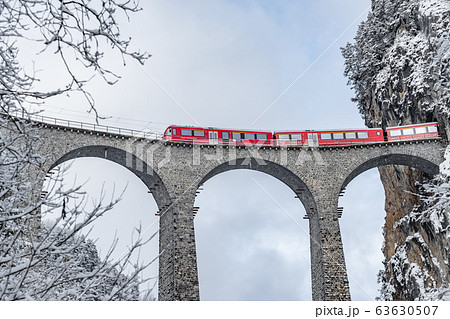 The Landwasser Viaduct with famous train of red color at winter time, landmark of Switzerland, snowing, Glacier express 63630507